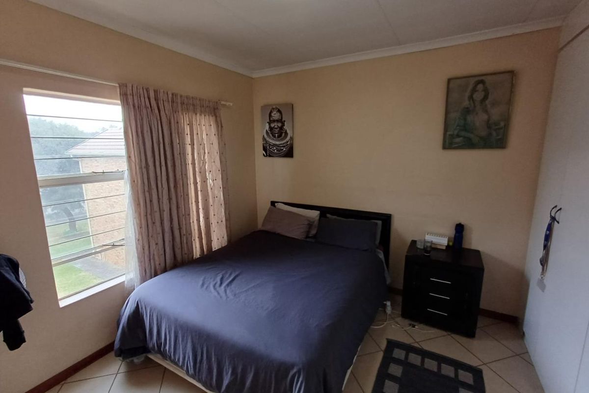 A functional bedroom featuring tiled flooring, a built-in wardrobe, and a large louvre window providing natural light.
