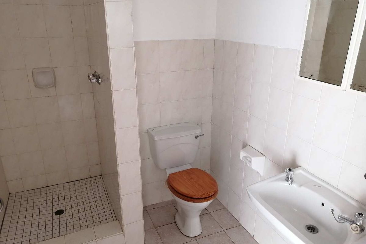 A dated bathroom featuring a tiled shower enclosure, pedestal basin, and toilet, requiring cosmetic updates to improve its overall condition and appeal.