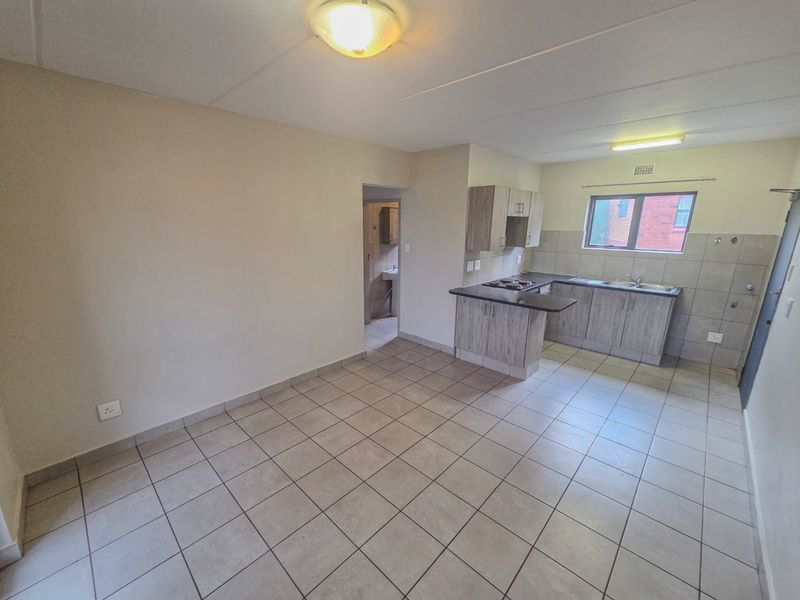 An open-plan living and kitchen area featuring tiled flooring, modern wood-look cabinetry, and a functional kitchen layout with a built-in hob and sink.