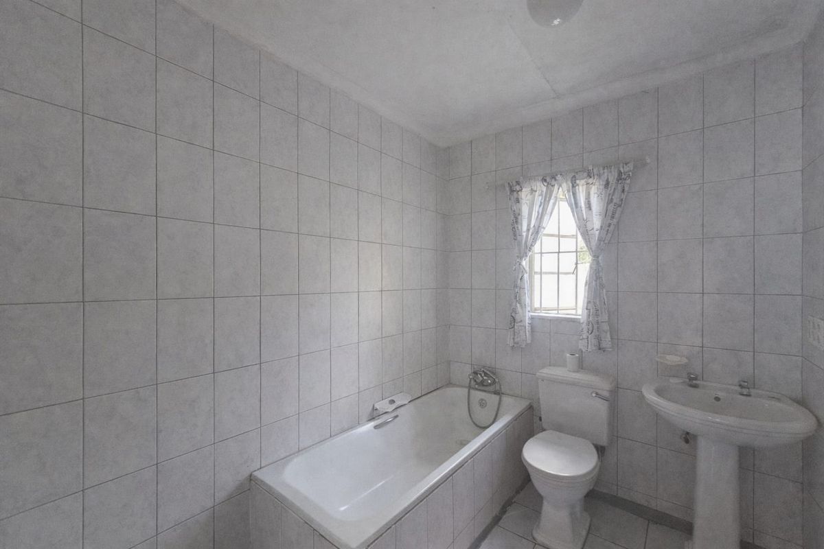 A functional bathroom featuring a standard bathtub, pedestal basin, and toilet, finished with full-height wall tiling and a small window for natural light.