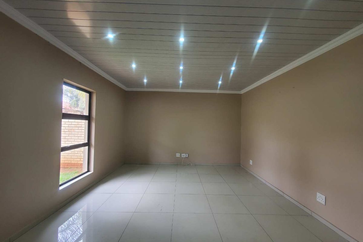 A spacious, empty living room featuring neutral wall tones, tiled flooring, and a modern ceiling with recessed downlighting.