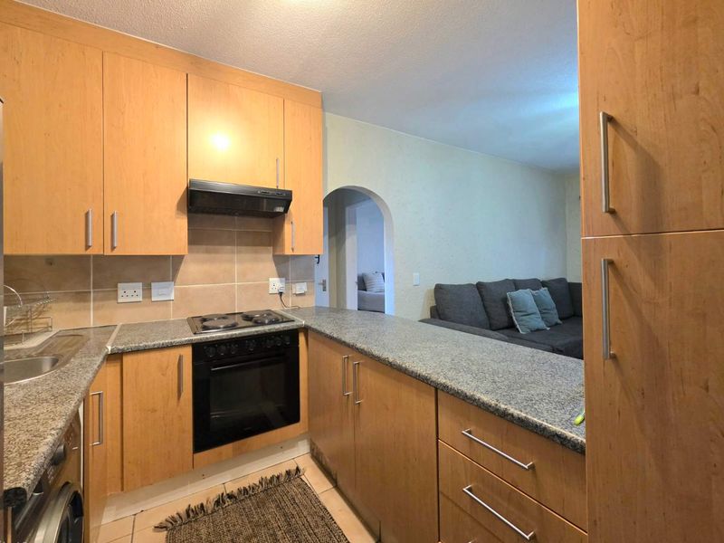 A functional kitchen featuring light wood cabinetry, granite countertops, and integrated appliances, with an open-plan layout leading into the living area.