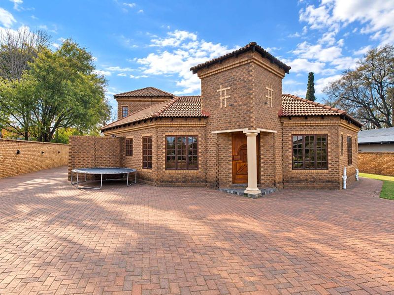 A well-maintained face brick house featuring a prominent entrance tower, tiled roof, and extensive paved driveway area.