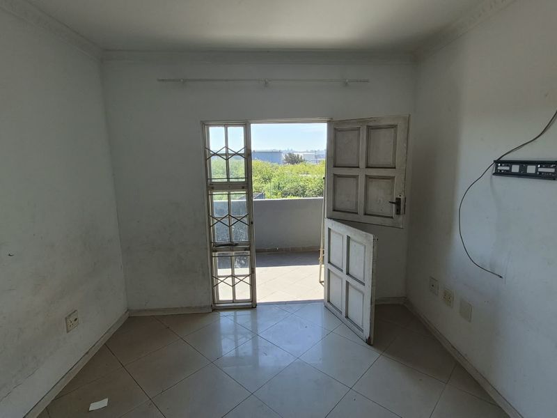 An empty living room featuring tiled flooring, coving, and direct access to a balcony through a security gate.