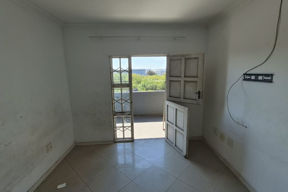 An empty living room featuring tiled flooring, coving, and direct access to a balcony through a security gate.