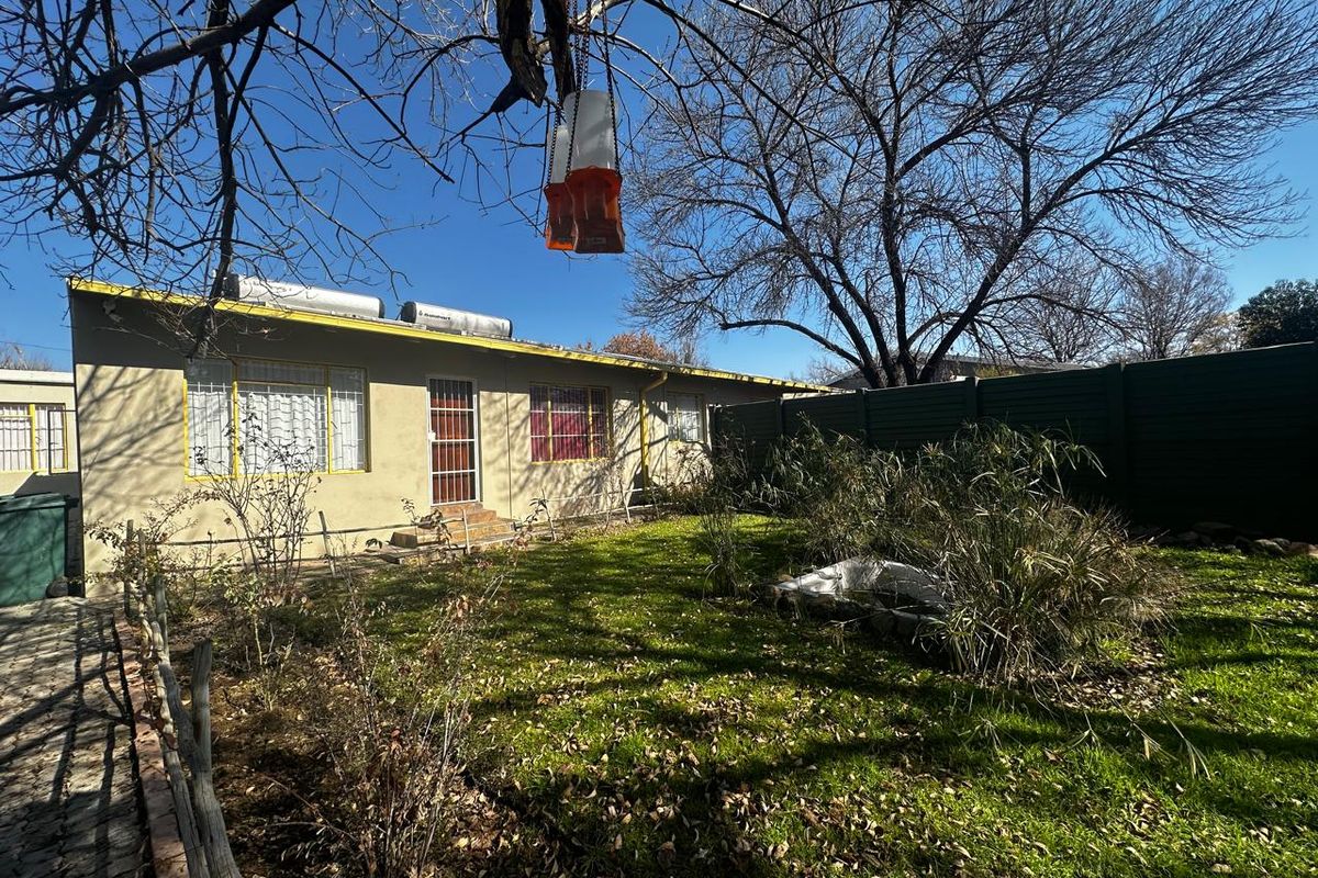 Rear view of the property featuring a garden area, solar water heating system, and security bars on windows and doors.