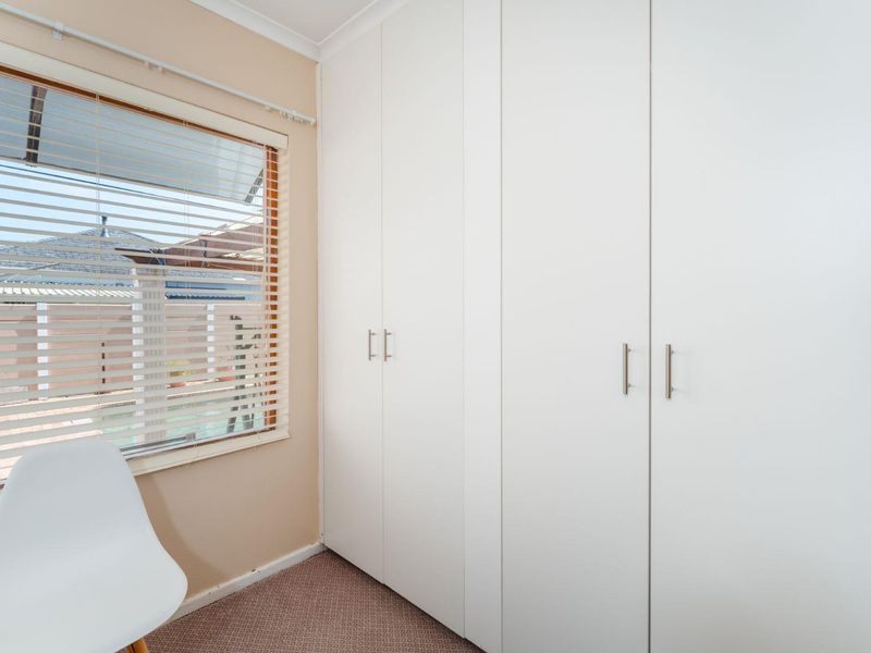 A bedroom featuring a large built-in wardrobe with white cabinetry and a window fitted with venetian blinds.