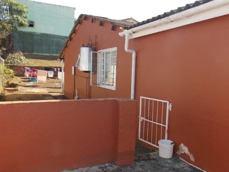 Rear exterior view of the property featuring a painted facade, external electric geyser, security gate, and perimeter precast concrete walling.