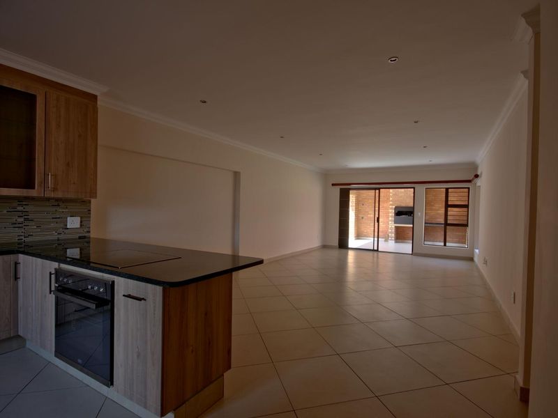 Spacious open-plan living area featuring a modern kitchen with granite countertops, built-in oven, and seamless flow to an outdoor patio with a built-in braai.
