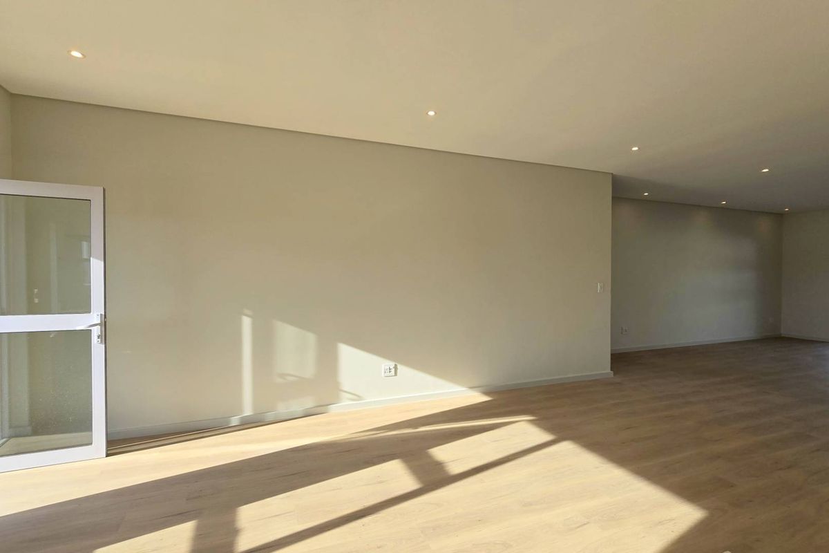 A spacious, bright, and empty living area featuring modern laminate flooring, recessed downlights, and large aluminium-framed glass doors leading to the exterior.