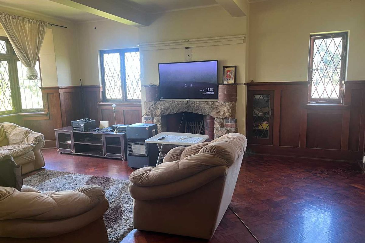 Spacious living room featuring original timber wall paneling, parquet flooring, and a prominent stone fireplace with leadlight windows.