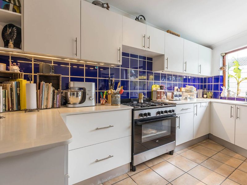 A functional kitchen featuring white cabinetry, stone countertops, a gas stove with oven, and a vibrant blue tiled backsplash.