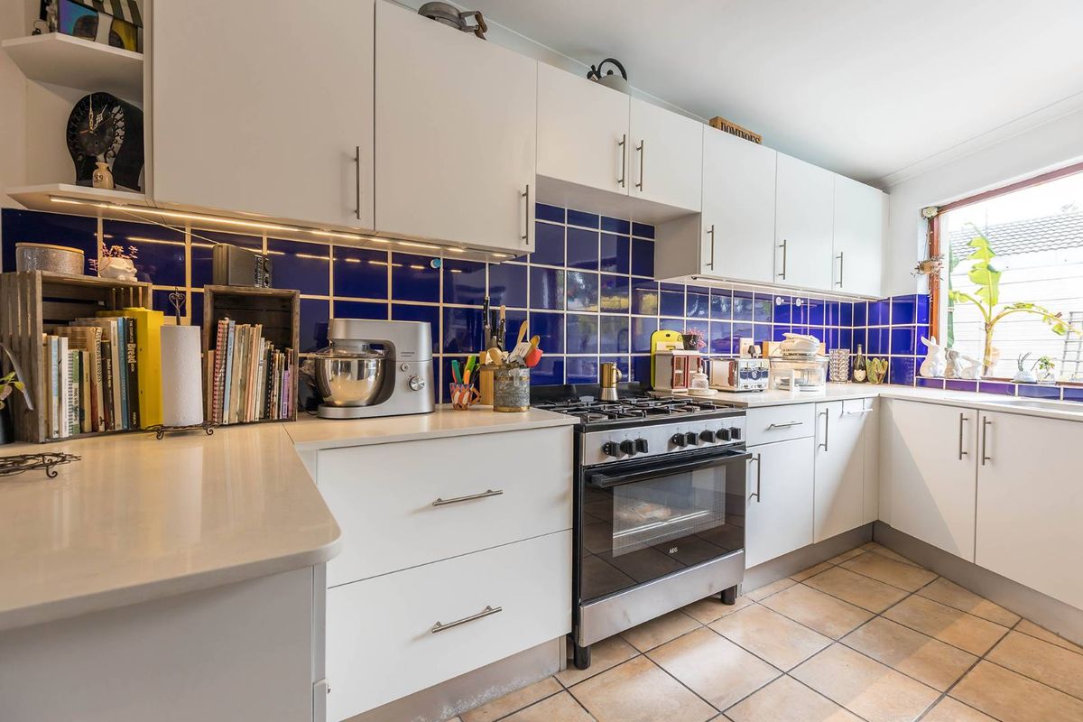 A functional kitchen featuring white cabinetry, stone countertops, a gas stove with oven, and a vibrant blue tiled backsplash.