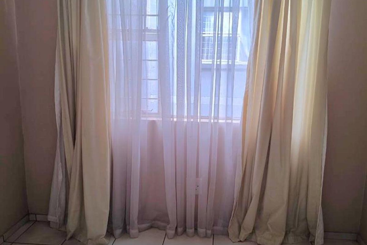 A simple bedroom featuring tiled flooring and a window with curtain tracks, providing a neutral and functional space.