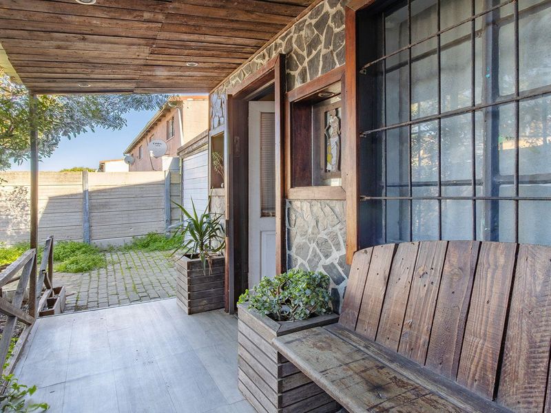 A covered patio area featuring stone wall cladding, timber ceiling, and direct access to a paved rear courtyard with boundary walling.