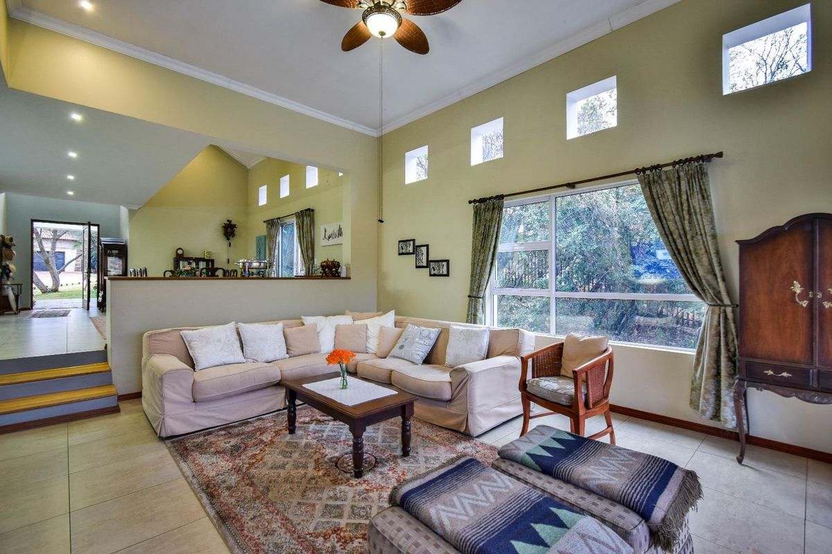 Spacious living room featuring high ceilings, clerestory windows, tiled flooring, and a ceiling fan, with an open-plan layout connecting to adjacent areas.