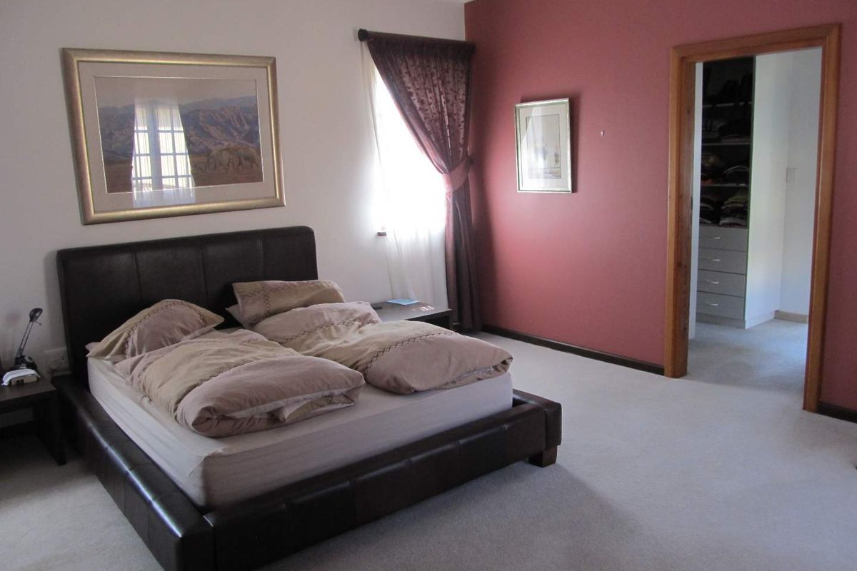 Spacious bedroom featuring neutral carpeting, a bold accent wall, and an adjoining walk-in closet with built-in shelving.