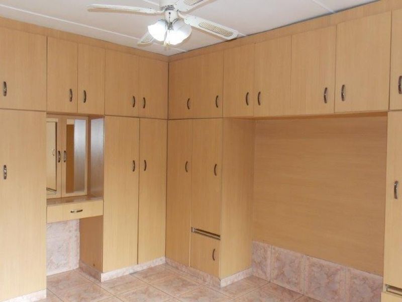 A bedroom featuring extensive built-in wooden cabinetry, a integrated vanity area, a ceiling fan, and tiled flooring.
