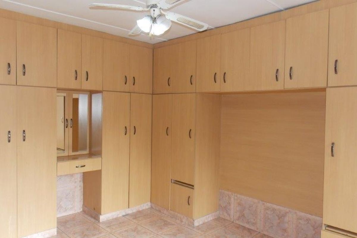 A bedroom featuring extensive built-in wooden cabinetry, a integrated vanity area, a ceiling fan, and tiled flooring.