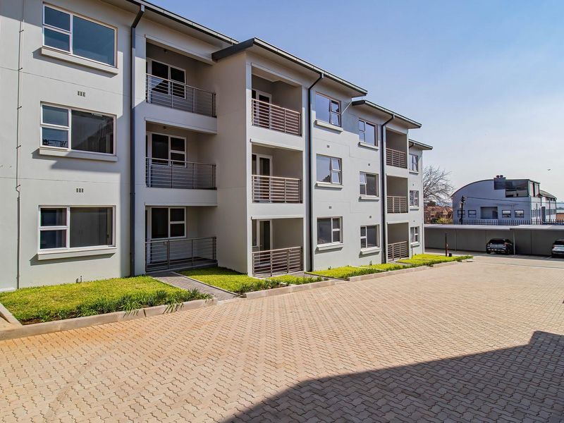 A modern apartment complex exterior featuring paved driveway access, private balconies with metal railings, and dedicated covered parking bays.