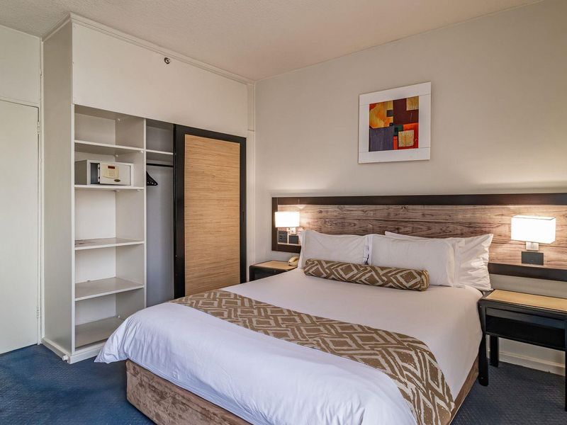 A bedroom featuring a built-in wardrobe with shelving and a wood-paneled headboard with integrated lighting.