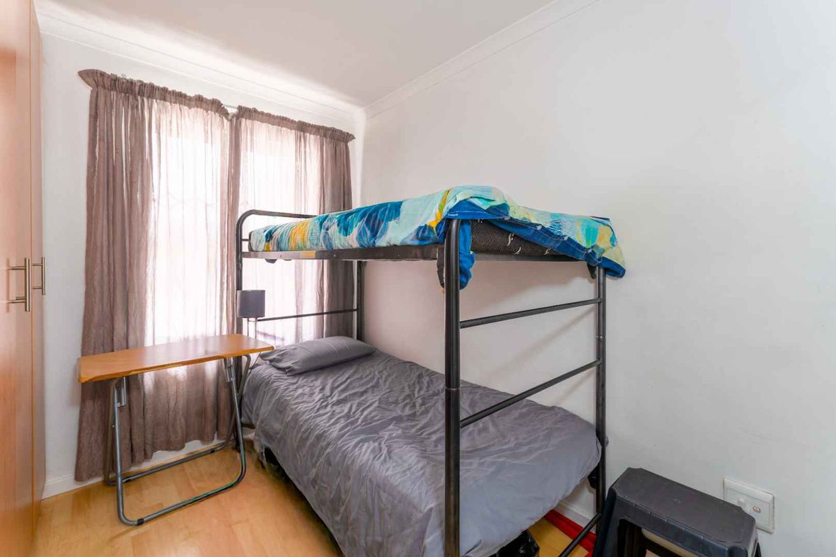 A compact bedroom featuring light wood-look flooring, built-in cabinetry, and a window with curtains.