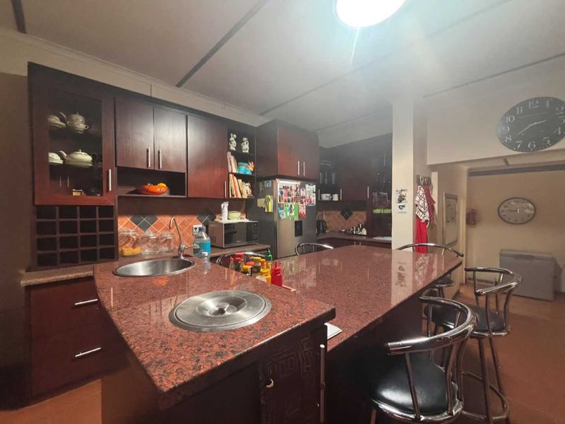 A functional kitchen featuring dark wood cabinetry, a large granite-topped island with an integrated sink, and a tiled backsplash.