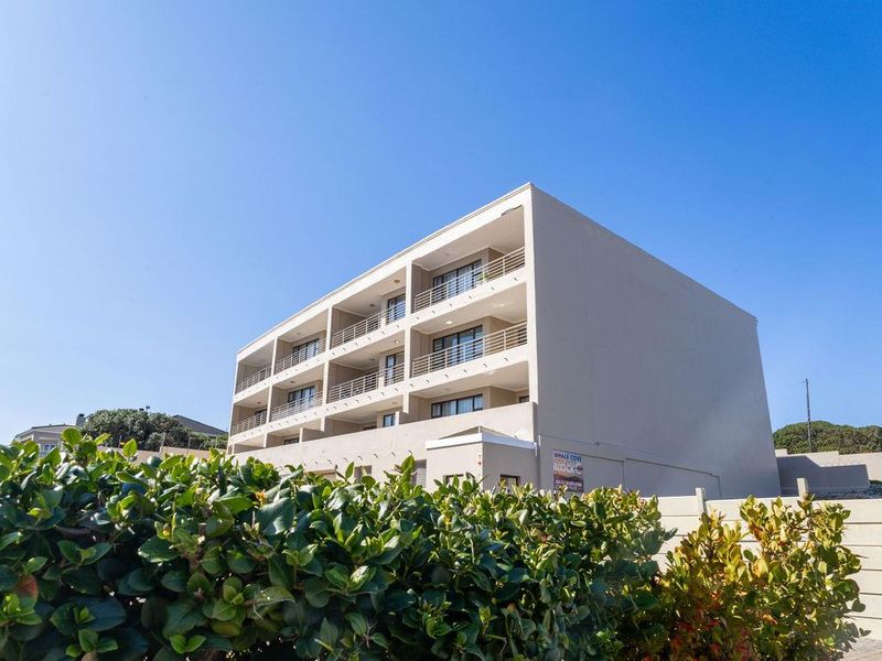 Exterior view of a multi-story apartment building featuring private balconies with metal railings and a clear blue sky.