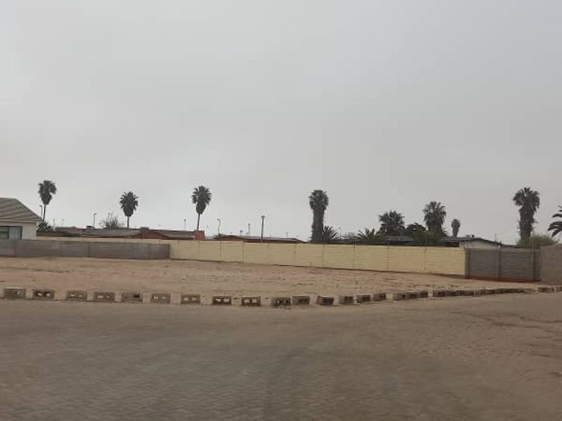 A vacant plot of land featuring a perimeter boundary wall and paved driveway access, offering a blank canvas for future development.