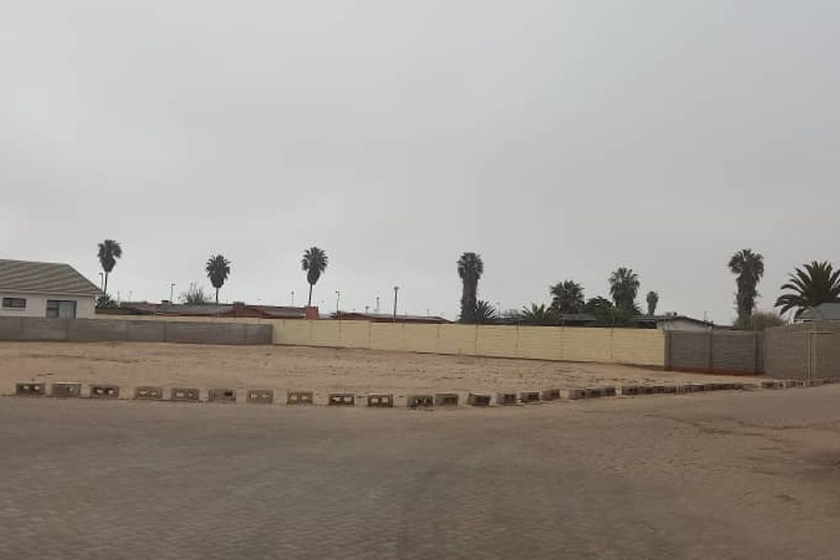 A vacant plot of land featuring a perimeter boundary wall and paved driveway access, offering a blank canvas for future development.