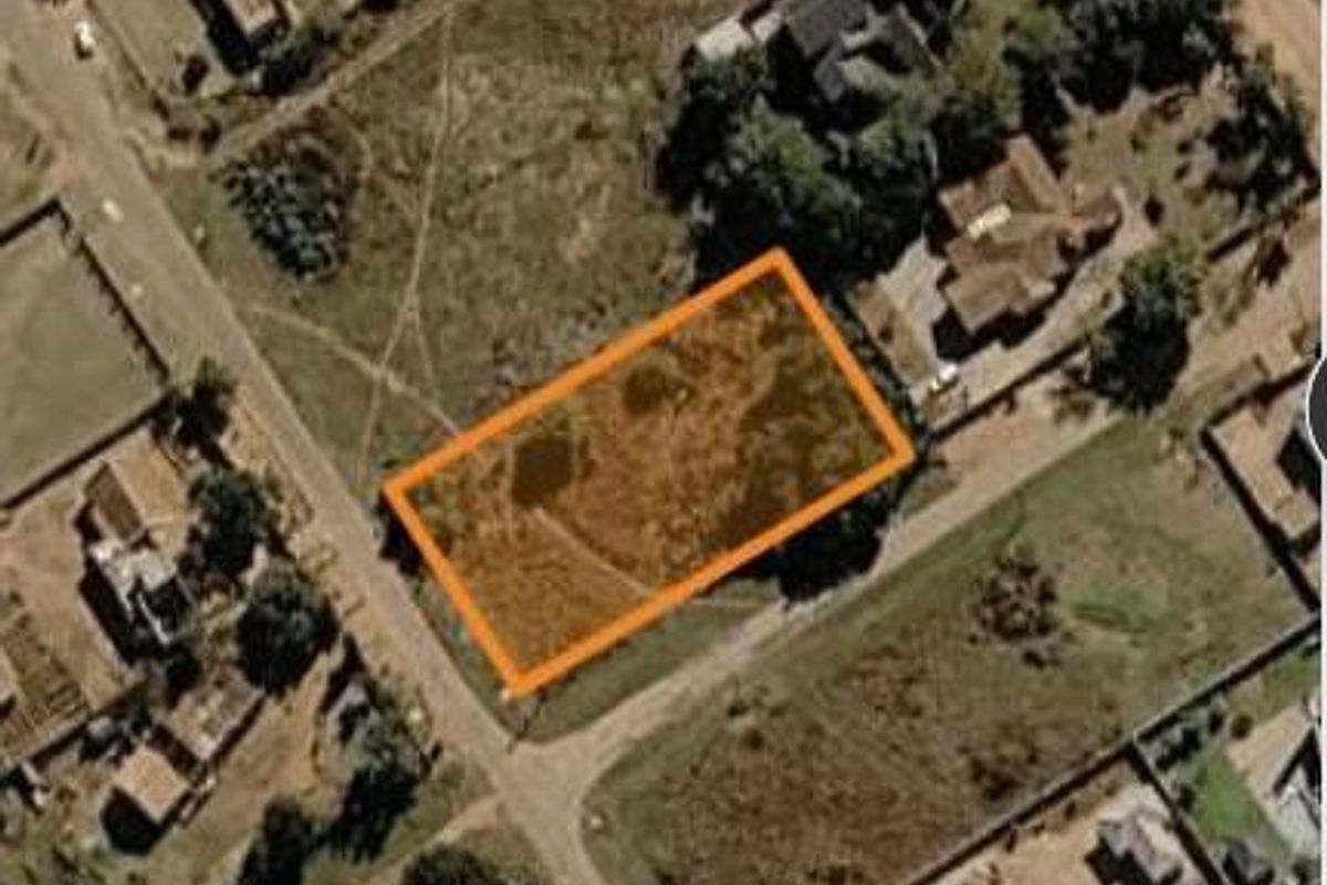 An aerial view of a vacant residential plot highlighted with an orange boundary, situated within an established neighborhood.