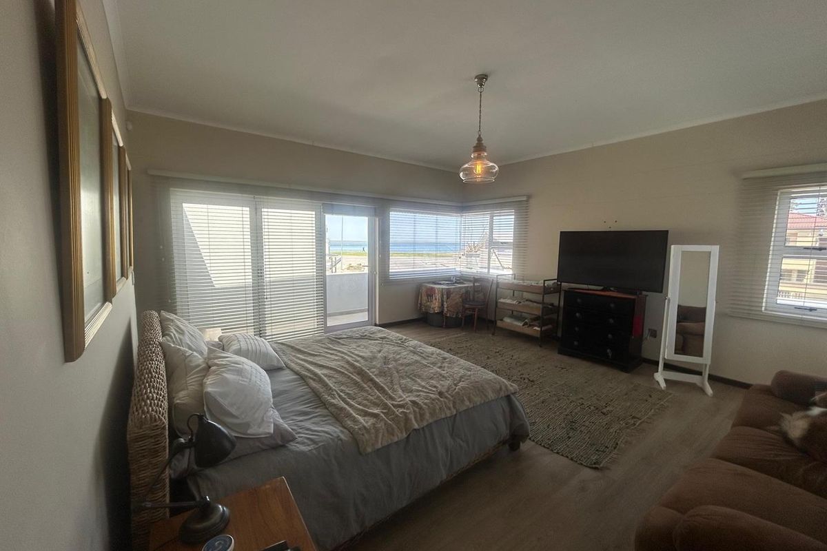 Spacious bedroom featuring light wood-look flooring, large windows with ocean views, and direct access to a private balcony.