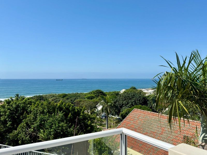 Elevated coastal view overlooking lush greenery and the ocean, featuring a modern glass balustrade in the foreground.