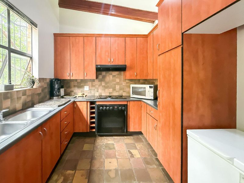 Functional kitchen featuring warm-toned cabinetry, stone countertops, built-in oven with gas hob, and a distinctive exposed timber ceiling beam.