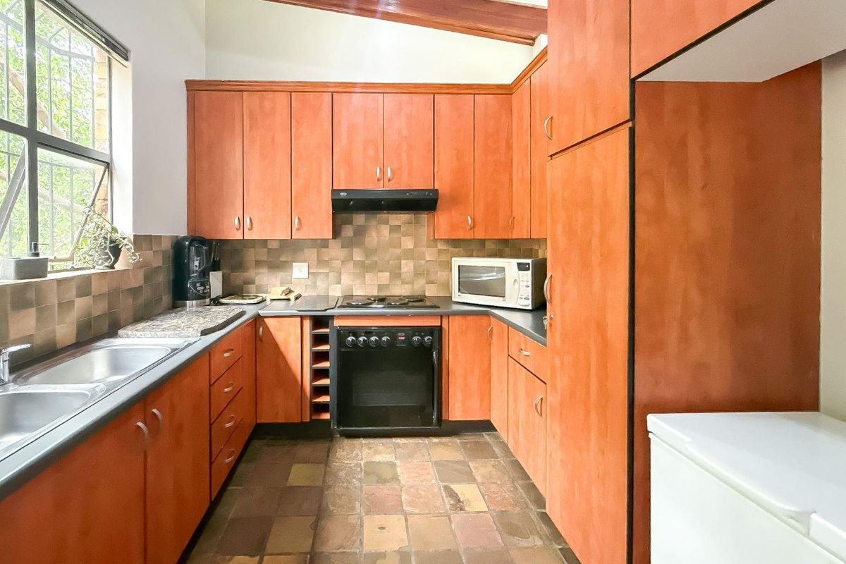 Functional kitchen featuring warm-toned cabinetry, stone countertops, built-in oven with gas hob, and a distinctive exposed timber ceiling beam.
