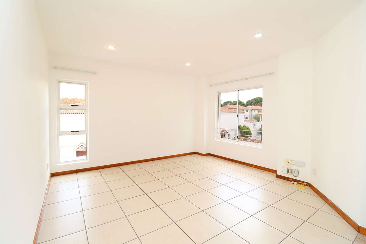 A bright, empty bedroom featuring neutral tiled flooring, recessed downlights, and large windows providing natural light and neighbourhood views.