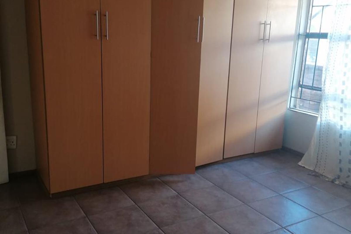 Bedroom featuring built-in wooden wardrobes, tiled flooring, and a window with security bars.