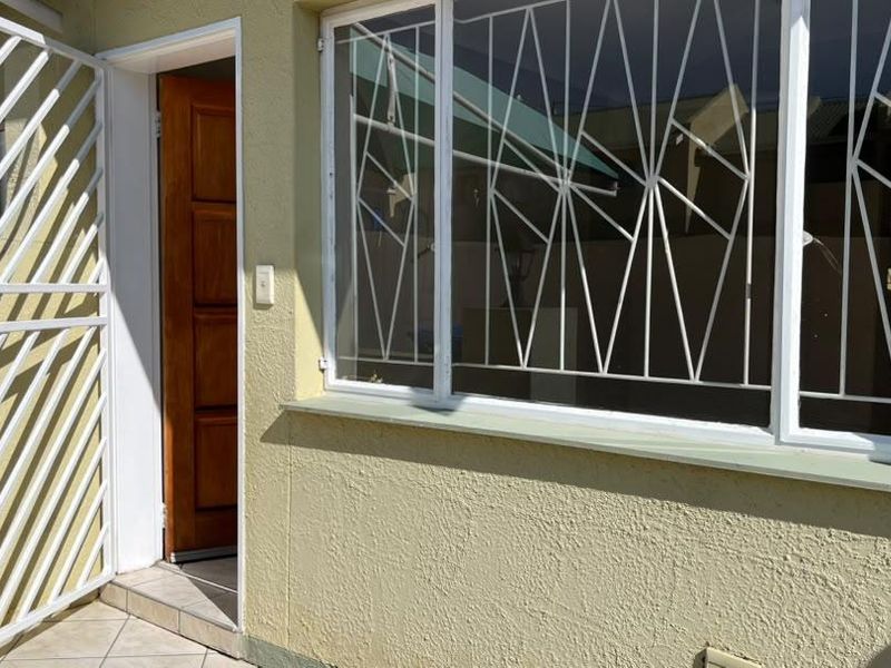 Front entrance of the townhouse featuring a timber door, security gate, and large window with protective security bars.