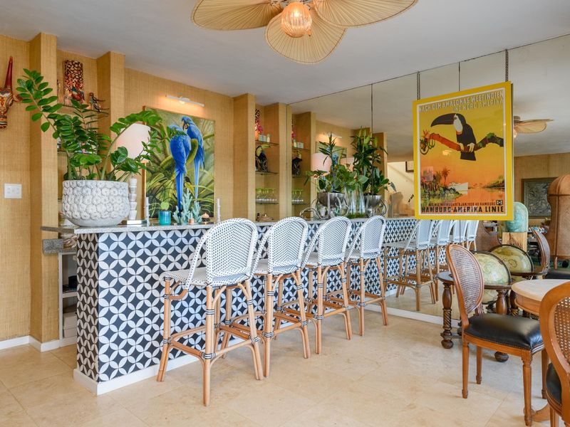 A stylish, well-appointed home bar area featuring a patterned tiled bar counter, stone top, built-in shelving, and a large mirrored wall.