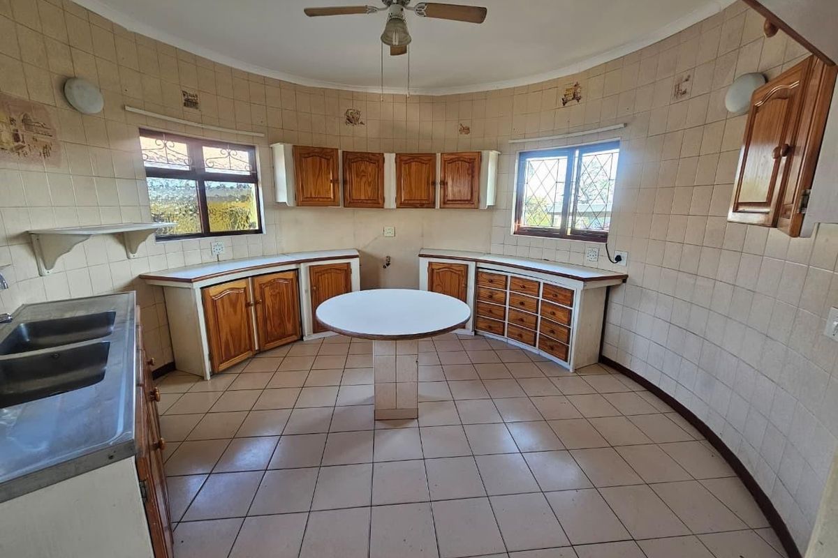 A spacious, circular-layout kitchen featuring dated wooden cabinetry, tiled surfaces, and a central island, offering significant potential for a modern renovation.