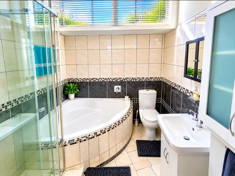 A well-appointed bathroom featuring a corner bathtub, separate glass shower enclosure, vanity basin, and neutral tiled finishes with decorative mosaic accents.