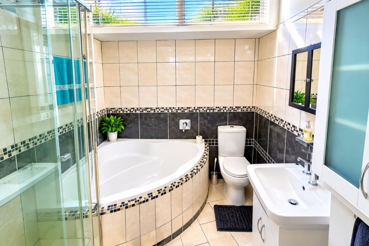 A well-appointed bathroom featuring a corner bathtub, separate glass shower enclosure, vanity basin, and neutral tiled finishes with decorative mosaic accents.