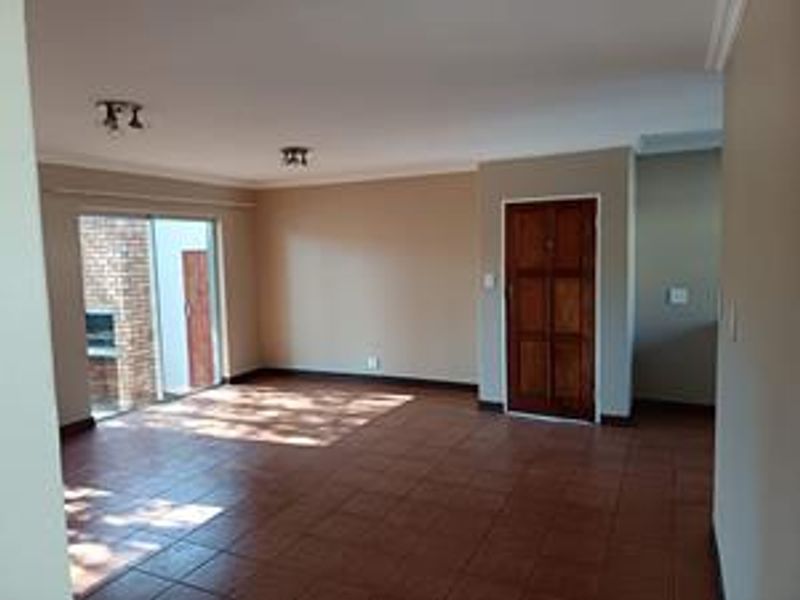 Spacious, empty living area featuring tiled flooring, neutral walls, and a sliding glass door leading to an outdoor area with a built-in fireplace.