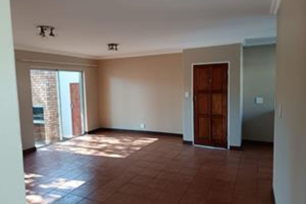 Spacious, empty living area featuring tiled flooring, neutral walls, and a sliding glass door leading to an outdoor area with a built-in fireplace.
