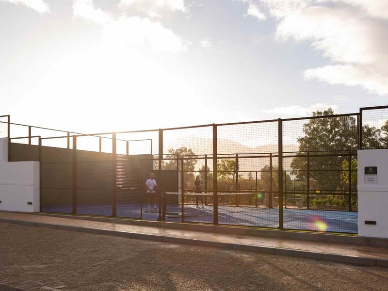 A well-maintained outdoor padel court facility featuring professional fencing and court surfacing, situated in a residential estate setting.