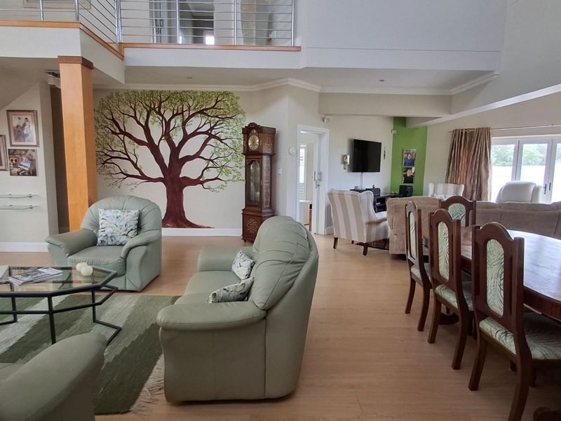 Spacious open-plan living and dining area featuring a double-volume ceiling, staircase with stainless steel balustrade, and direct access to the patio through glass doors.