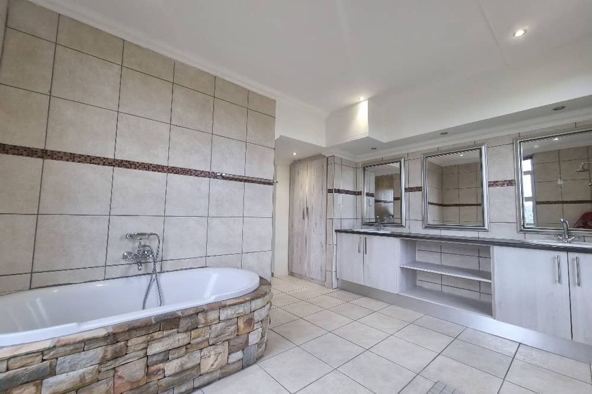 Spacious bathroom featuring a stone-clad built-in bathtub, double vanity with integrated mirrors, and neutral floor-to-ceiling tiling.