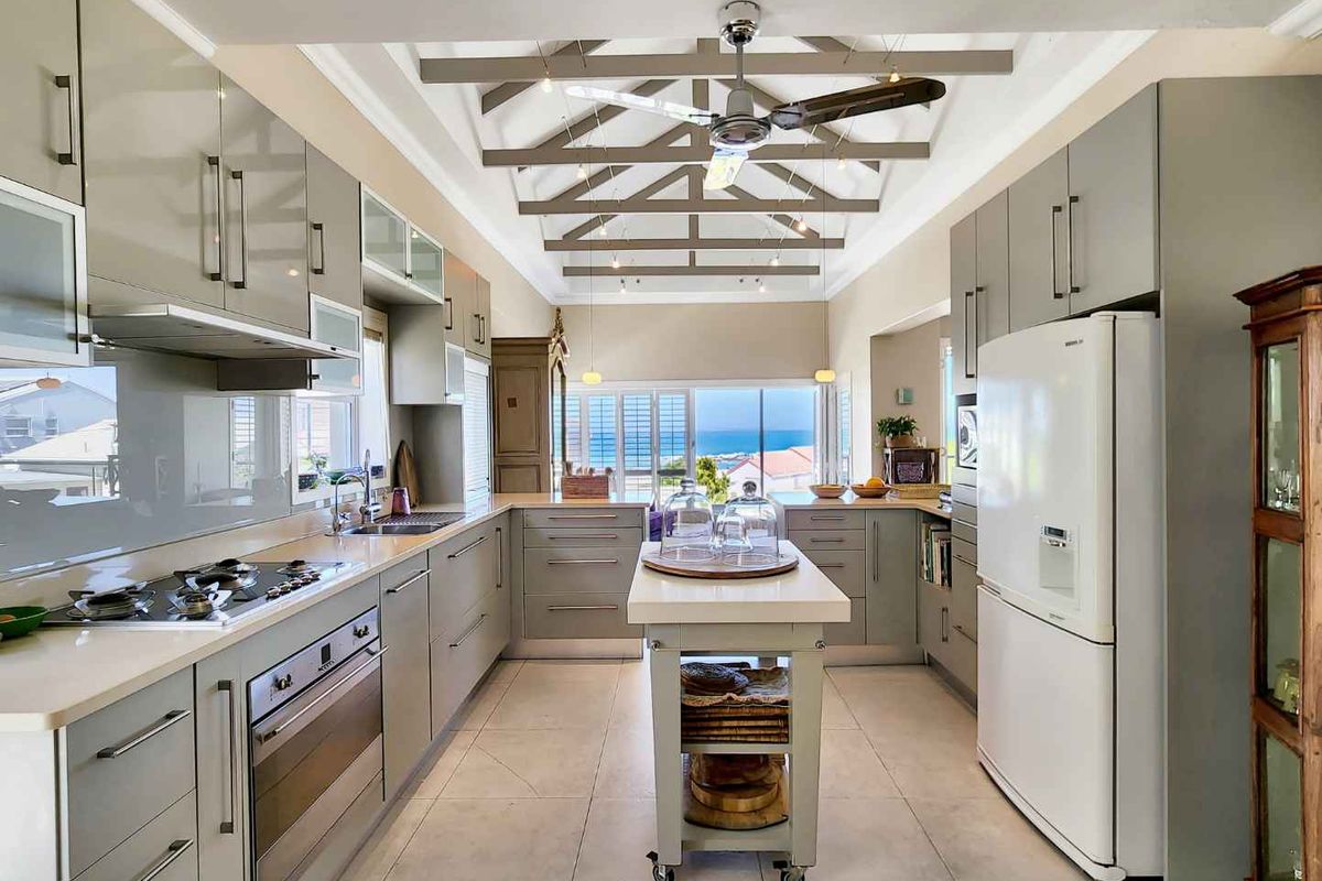 Modern kitchen featuring sleek cabinetry, stone countertops, integrated appliances, and a vaulted ceiling with exposed beams, offering a bright and functional culinary space.