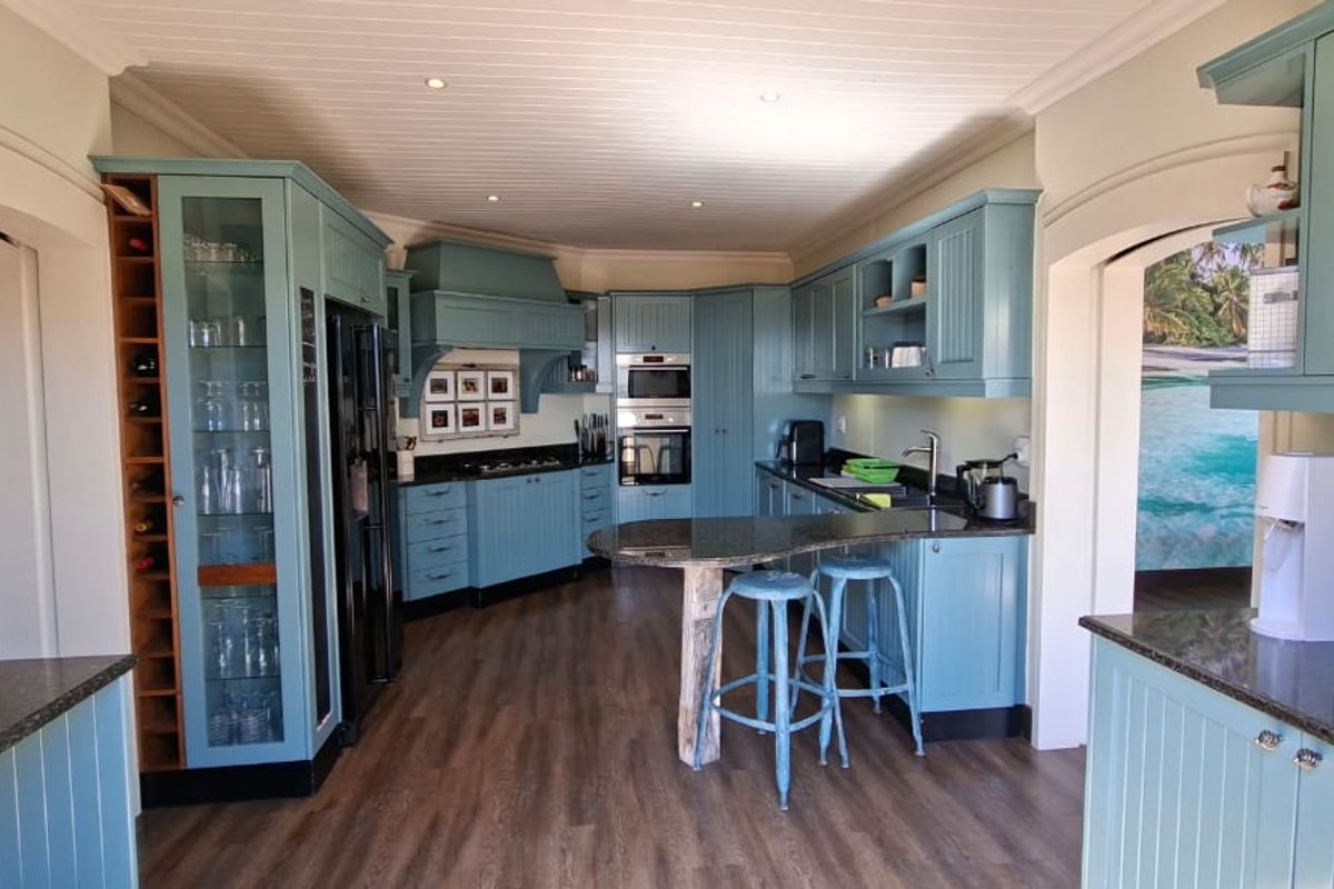 A well-appointed kitchen featuring custom blue cabinetry, granite countertops, integrated appliances, and a central breakfast bar with a unique wooden support.