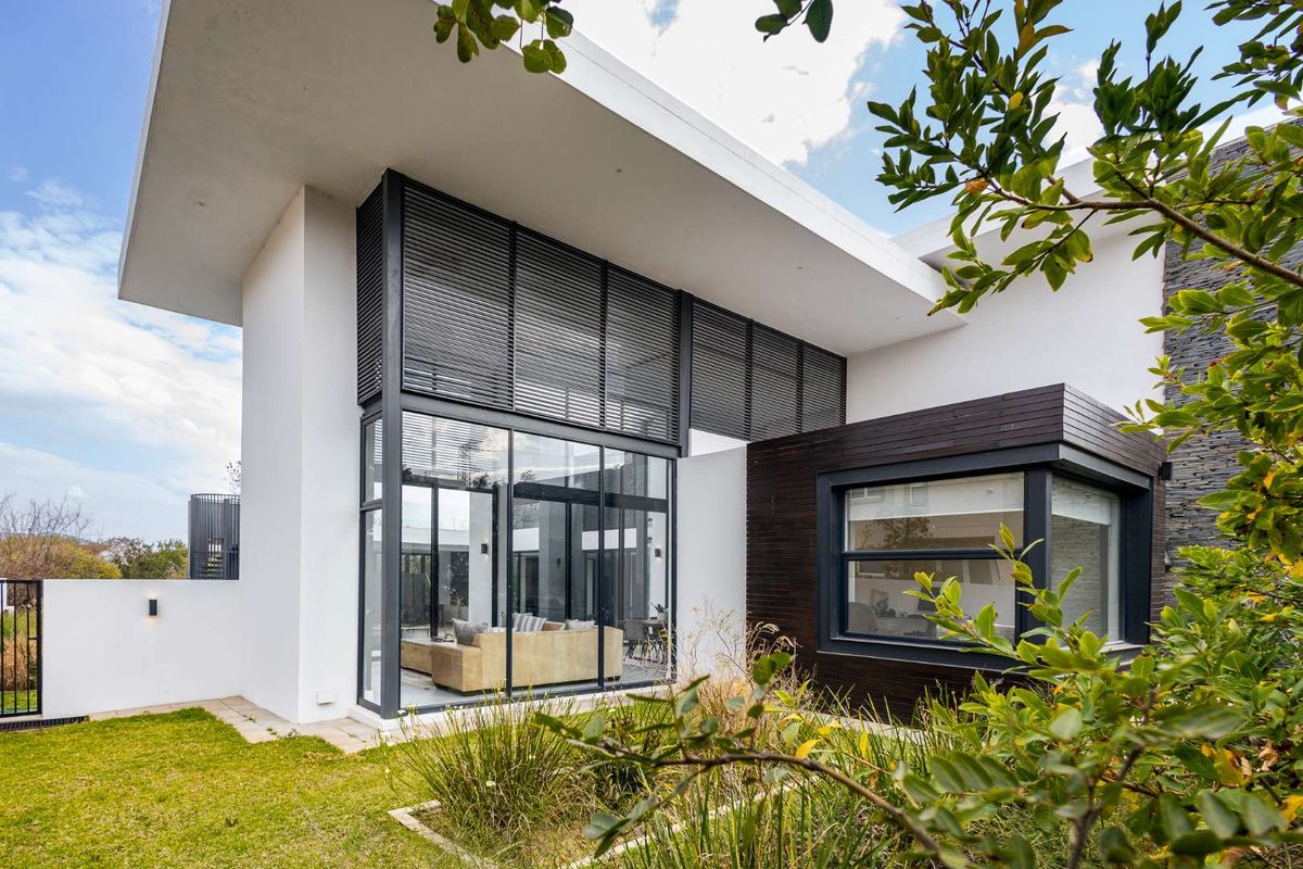 Modern architectural rear elevation featuring expansive floor-to-ceiling glass windows, sleek dark timber cladding, and a well-maintained garden area.